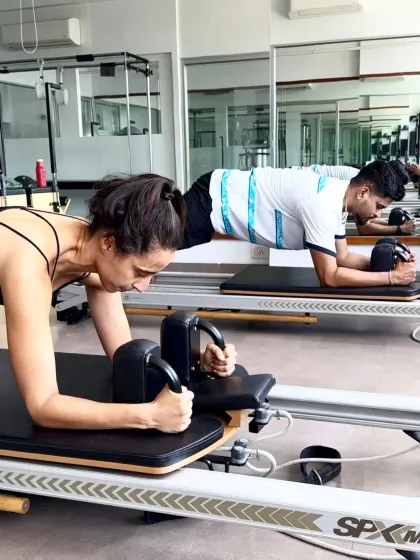 Namrata Purohit and Shreyas Iyer hold a synchronized plank on the reformer. This demonstrates the core strength and endurance that Pilates builds, which is the foundation of all athletic movement.