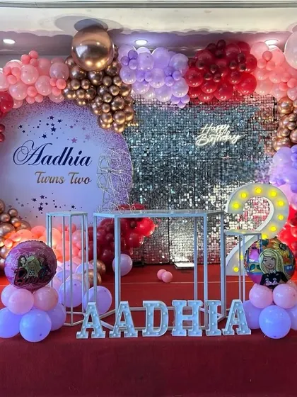 A grand setup for a second birthday party. This decoration features a large balloon arrangement in shades of pink and rose gold, a shimmer wall, and a personalized circular backdrop.