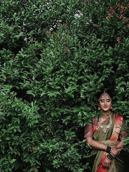An artistic portrait of the bride standing against a large green bush, looking serene and beautiful.