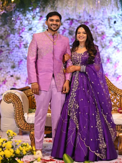A full-length portrait of the couple on their reception stage. The bride's entire look, from the purple lehenga to the soft glam makeup, is cohesive and beautiful.