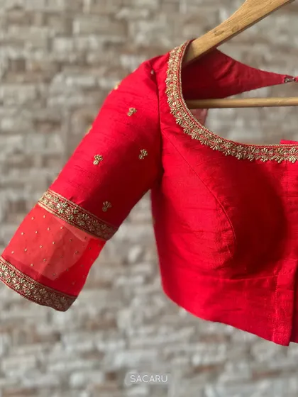 The quintessential red saree blouse. This piece is crafted from raw silk and features delicate gold embroidery along the neckline and a sheer panel on the sleeve.