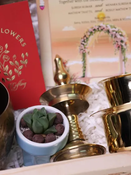 A close-up of a luxurious wedding invitation hamper I designed. It includes traditional elements like a brass nilavilakku and a succulent, setting a tone of elegance and warmth.