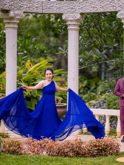 A fun, dynamic shot within the white pillar structure. The bride-to-be playfully holds out her flowing blue gown, adding a sense of movement and joy to this pre-wedding portrait.