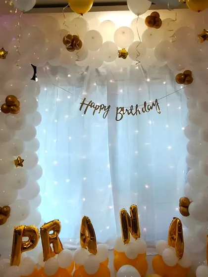 A closer view of the white and gold personalized balloon arch, showing the detail of the star-shaped foil accents.