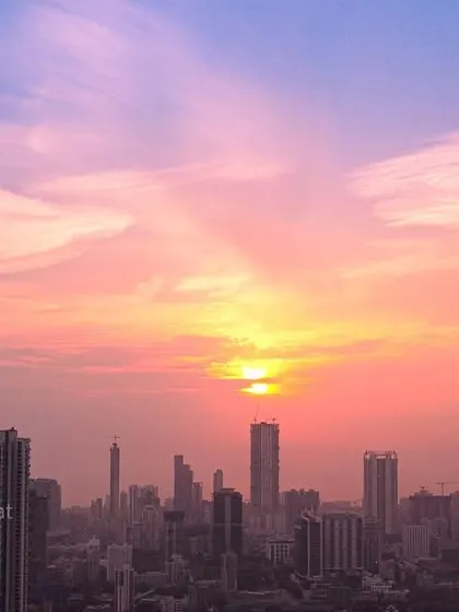 The Mumbai skyline is captured under a beautiful sunset, with the sky filled with pink and orange hues and wispy clouds.