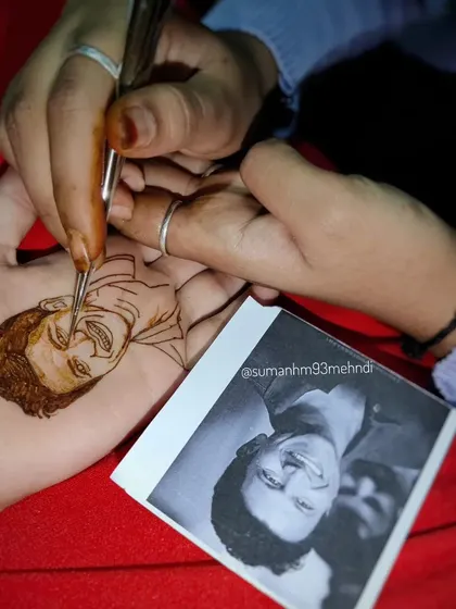 Here you can see the artist's hand at work, carefully drawing the fine details of a portrait with a henna cone. Each stroke is deliberate and precise.