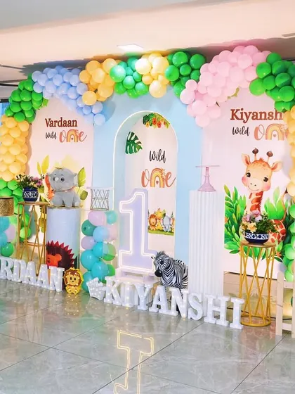 Another view of the jungle theme for twins, this wide shot shows the full stage with two personalized backdrops, large animal props like a giraffe and elephant, and light-up names.