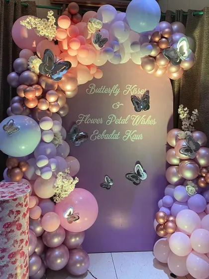 A "Butterfly Kisses & Flower Petal Wishes" themed party. This setup features a beautiful pastel purple and pink balloon arch on a custom backdrop.