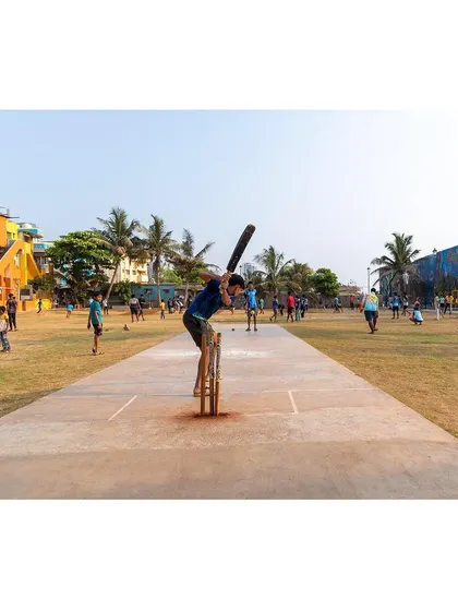 A batsman in action on the cricket pitch at the Worli ground. The design provides a dedicated, level pitch that serves as the centerpiece for the community's most popular sport.