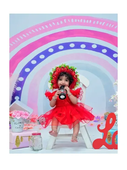 This little one, dressed in a vibrant red outfit with a floral bonnet, explores the props in a rainbow-themed setup. I love capturing their natural curiosity during these portrait sessions.