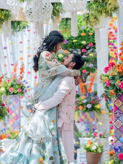 A romantic lift! The groom lifts his bride amidst the colorful floral decor of their Mehendi carnival.