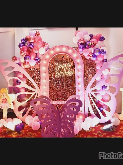 A first birthday home setup with a butterfly theme. This decor features a rose gold sequin wall, lighted butterfly wings, and marquee letters, showing how we can create a grand look in any space.