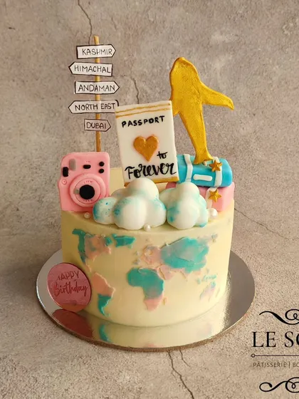 This cake celebrates a love for travel. The half-kg Chocolate Truffle cake features a world map texture, a passport, a camera, and a signpost pointing to favorite destinations.