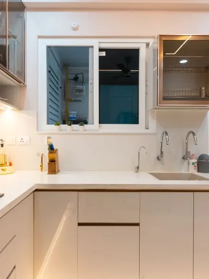 A beautifully lit U-shaped kitchen in a soft beige. The glass-fronted dish-drying cabinet above the sink is a practical and stylish feature.