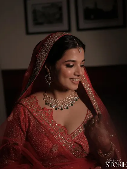 A soft and smiling portrait of a bride in her red lehenga. The makeup is clean and minimal, with a focus on radiant skin and delicately defined eyes, perfect for a classic wedding look.