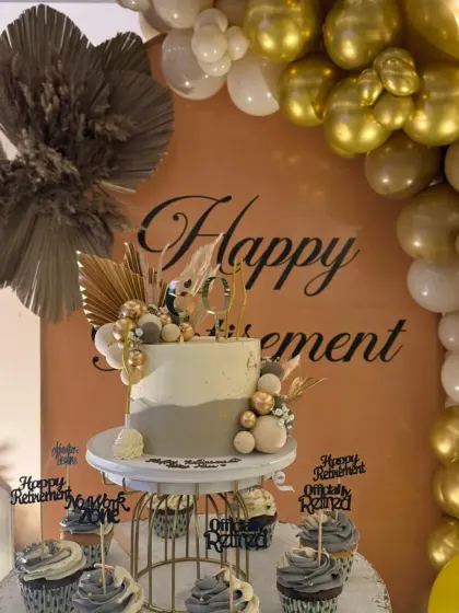 The dessert table was a highlight of the retirement party. It featured a stunning cake and cupcakes that matched the theme, complete with a "Happy Retirement" backdrop and boho-chic dry pampas grass accents.