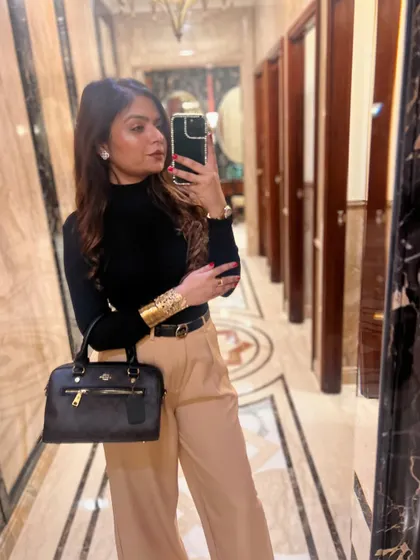 A mirror selfie showcasing a chic winter look with a black turtleneck and beige trousers.