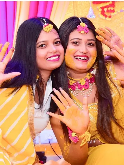 Fun and smiles at a Haldi ceremony, as the bride and her friend show off their turmeric-covered hands.