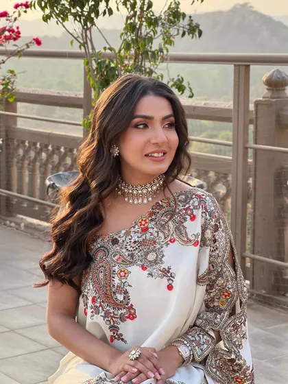 A bride at her Mehandi, her hair in soft, flowing waves that complement her elegant one-shoulder saree.