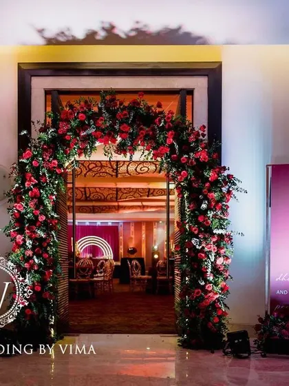 A bold and luxurious reception with a red and black color scheme. The decor includes rich red roses, modern crystal candelabras, and a stylish bar with a neon arch backdrop.