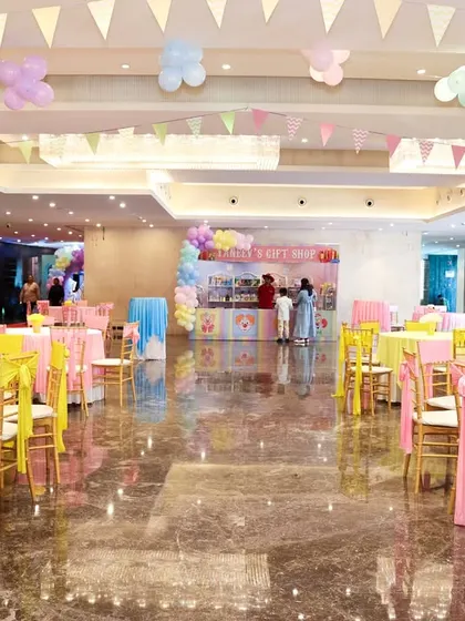 A wide view of the party hall, showing the colorful table settings and festive bunting hanging from the ceiling.