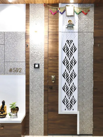 The safety door for this entrance features an intricate white jali panel set against a wood-finish door. The design combines traditional motifs with modern materials for a unique look.