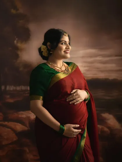 A painterly style portrait of a mother-to-be in a traditional saree, looking towards the future with a gentle smile. The backdrop gives the image a classic, artistic quality.