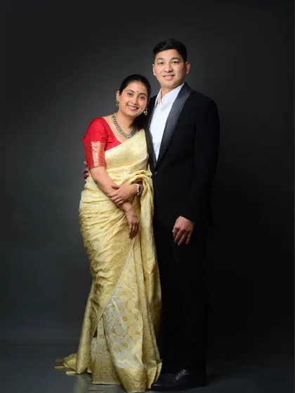 A full-length portrait of the couple in a classic pose, showing the beautiful drape of the saree and the sharp tailoring of the suit.