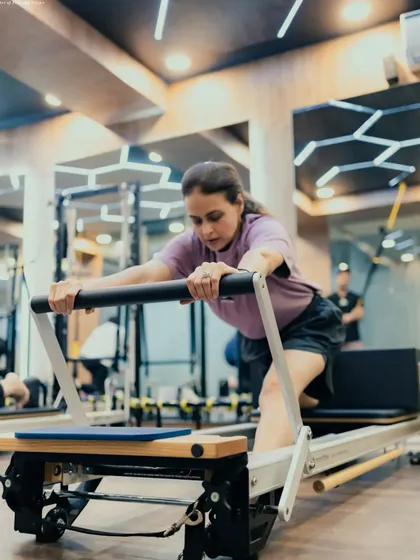 A focused client performs a deep stretch on the Reformer, a move that requires core engagement to maintain balance and control.