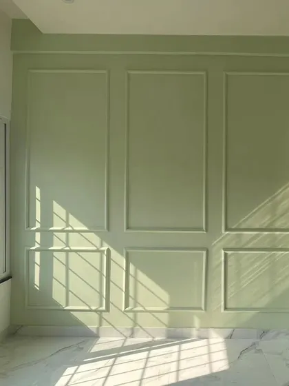Sunlight streams into this room, highlighting the freshly painted sage green wall with classic panel molding. This photo captures the beautiful interplay of color, texture, and natural light during the finishing phase.