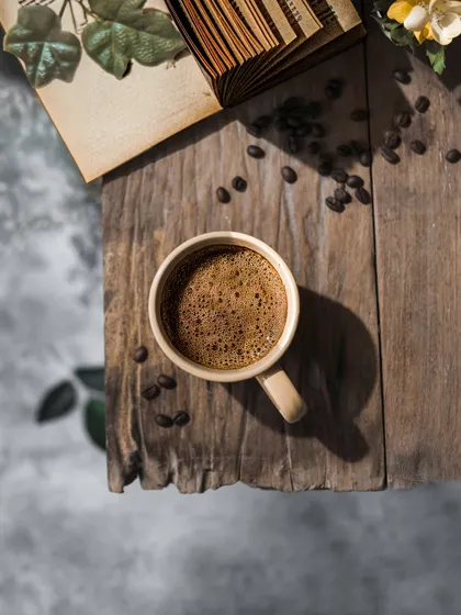 A flatlay of a cup of coffee on a rustic wooden plank, surrounded by an old book and coffee beans. This shot captures a perfect moment of quiet reflection.