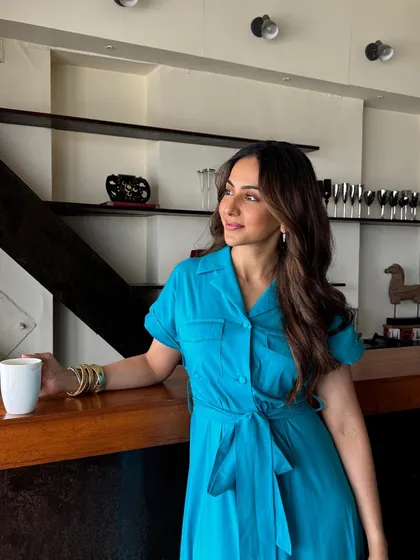 A full-length look at Rakul Preet Singh enjoying her coffee in a chic blue dress, perfectly complemented by her Upakarna bangle stack. Style that’s comfortable and confident.