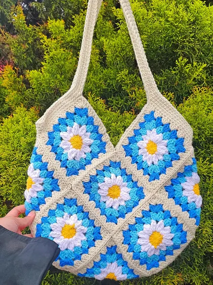 A full view of the Daisy Tote held against a natural background, making the blue and yellow floral pattern pop. This bag is constructed from 13 individual granny squares that I join by hand.