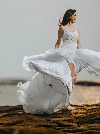 A bridal portrait full of movement and life. The bride's dress is caught by the sea breeze, creating a dynamic and free-spirited image against the ocean backdrop.