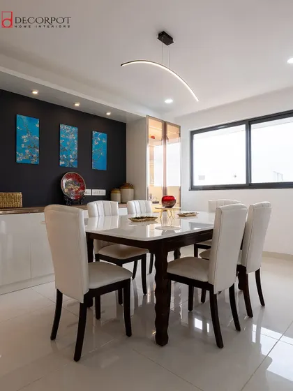 A modern dining room with a sleek white-top table and matching leather chairs. A dark accent wall with minimalist art provides a beautiful contrast, while a curved pendant light adds a contemporary touch.