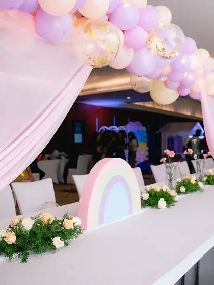 The guest seating for the unicorn party featured long tables decorated with pastel rainbow cutouts, floral arrangements, and balloon arches overhead.