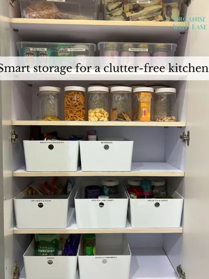 Smart storage for a clutter-free kitchen. This pantry cabinet uses clear jars for snacks on one shelf and labeled white bins for other categories, creating a clean and orderly system.