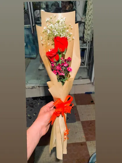 A rustic hand-tied bouquet with two red roses and other small filler flowers. The simple brown paper wrapping makes it a charming and understated gesture.