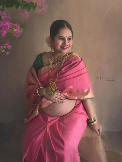 Radiating joy and serenity, this close-up portrait in a pink Kanchipuram saree highlights the beautiful glow of pregnancy. The traditional temple jewelry and floral hairpiece complete this classic, ethnic maternity look.
