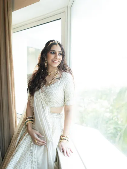 A beautiful bridal portrait in a white lehenga, bathed in natural light from a large window. Her happy expression and the bright, airy feel make this a lovely shot.