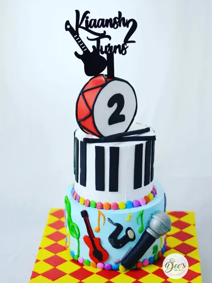 A fun and colorful music-themed cake for a second birthday. This cake has it all: a piano, a drum, a guitar, and a microphone.