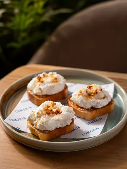 A close-up of the Cheeni Malai Toast at Comorin. This simple, clean shot focuses on the texture of the food, presented on custom branded paper that reinforces the restaurant's identity.