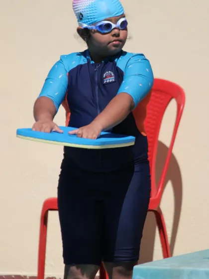 A young girl practices her posture with a kickboard before entering the pool. We incorporate dry-land exercises to help build muscle memory for correct swimming form.
