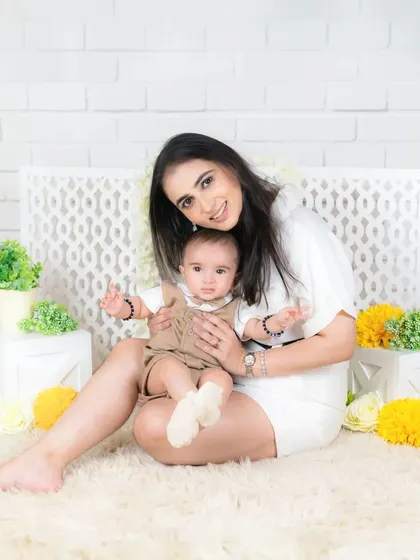 A mother holds her baby boy in her lap, both smiling for the camera. The clean, white setting makes their happy expressions pop.