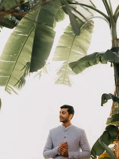 A portrait of the groom, looking thoughtful and dapper amidst a backdrop of lush banana leaves. This shot captures a quiet moment of anticipation.