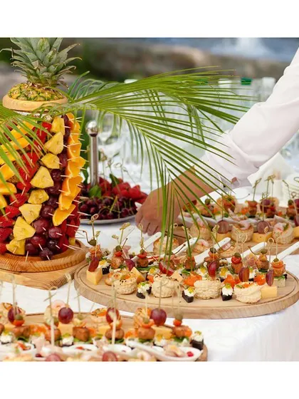 A tropical-themed fruit and appetizer station. This setup features a pineapple fruit tree and a variety of canapés, perfect for adding a fresh and vibrant touch to a summer corporate event.