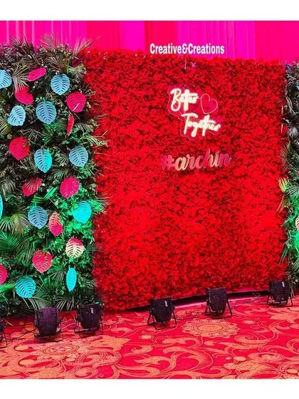 A unique photo wall with a central red rose panel flanked by green walls with colorful leaf cutouts. This design is modern, artistic, and perfect for an outdoor event.