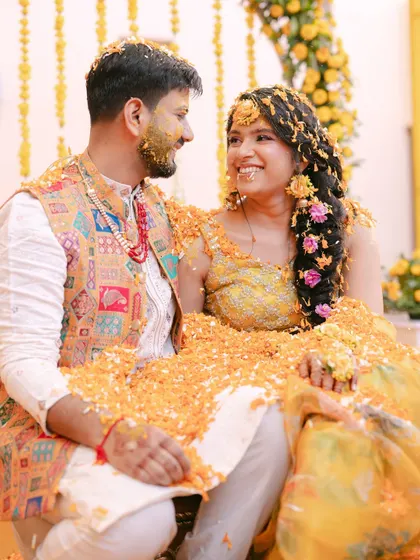 A sweet, candid moment between the couple during their Haldi ceremony, covered in marigold petals and sharing a happy, loving gaze.
