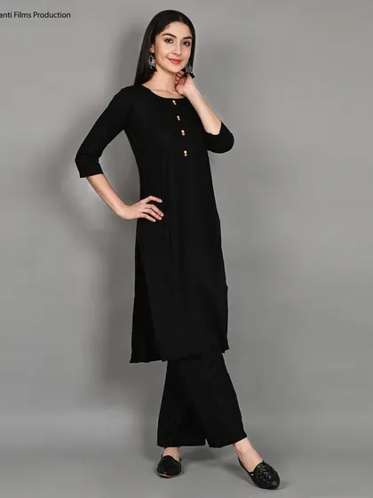 A classic three-quarter pose for a simple black kurti and palazzo set. This shot is a staple for e-commerce, providing a clear and flattering view of the outfit on a neutral grey background.