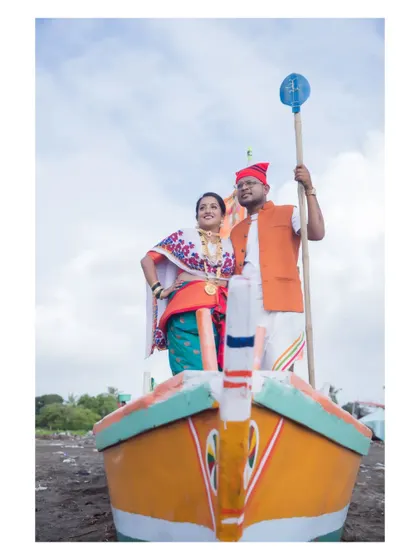 A powerful, full-length portrait of the couple on the boat, showcasing their traditional Koli attire and the vibrant colors of the setting.